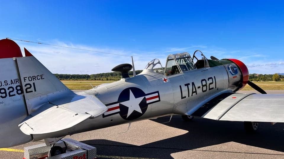 A T-6 Texan aircraft with a silver and red paint scheme parked on the tarmac.
