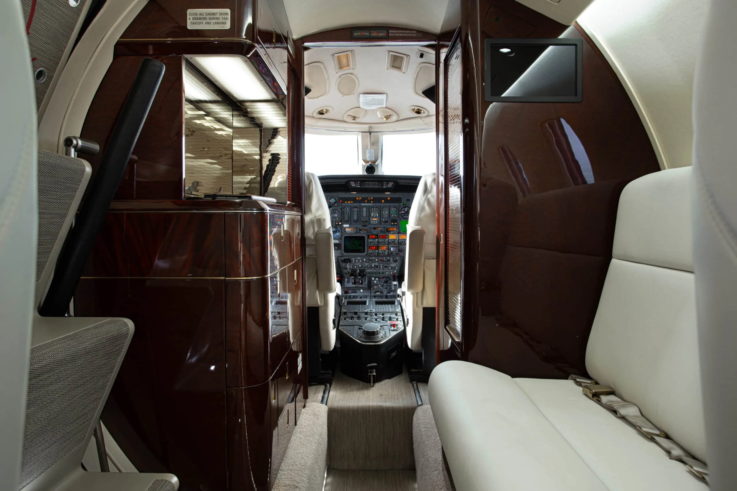 View from the aircraft cabin looking forward into the cockpit, showing dark wood paneling and a small screen.