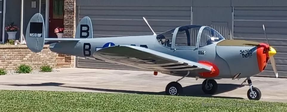 A grey single-engine aircraft with a red nose and "Sassy Baby" text is parked on a concrete driveway.