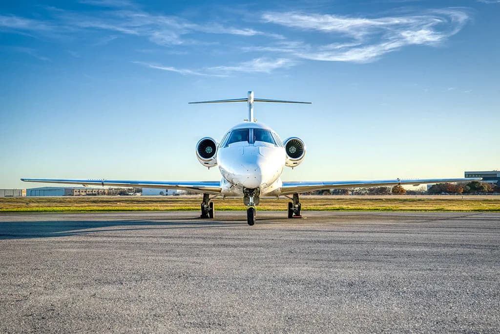 A white business jet (N24KT) is viewed head-on, parked on a tarmac under a clear blue sky.