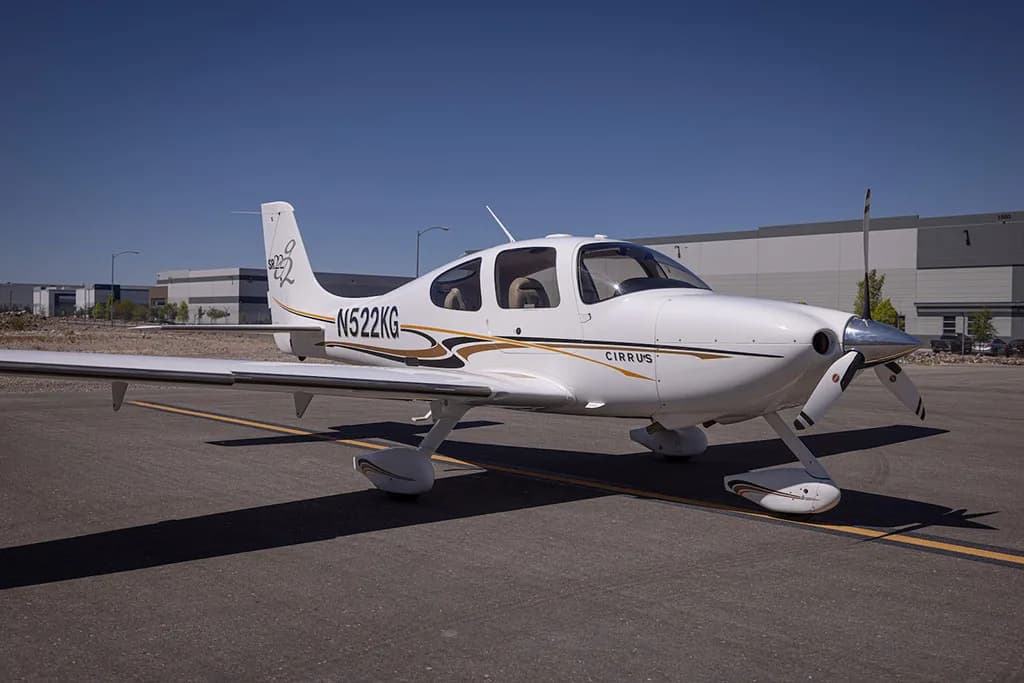 A white Cirrus SR22 aircraft with gold and black stripes, registration N522KG, parked on an airfield.