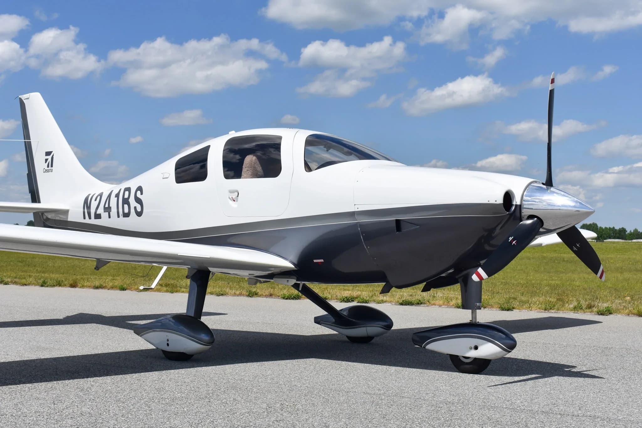 A front-side view of a white and dark grey Cessna TTx (Corvalis 400) aircraft, N241BS, parked on an airfield.