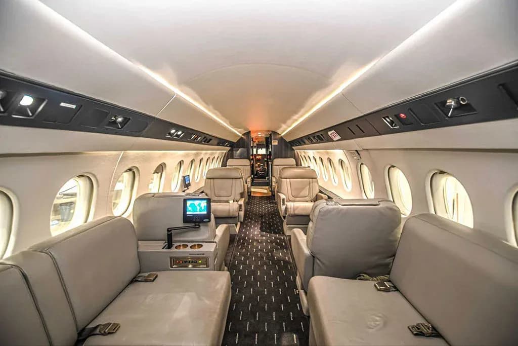 The luxurious interior cabin of the Dassault Falcon 900EX, showing light-colored seats and a forward-facing view.