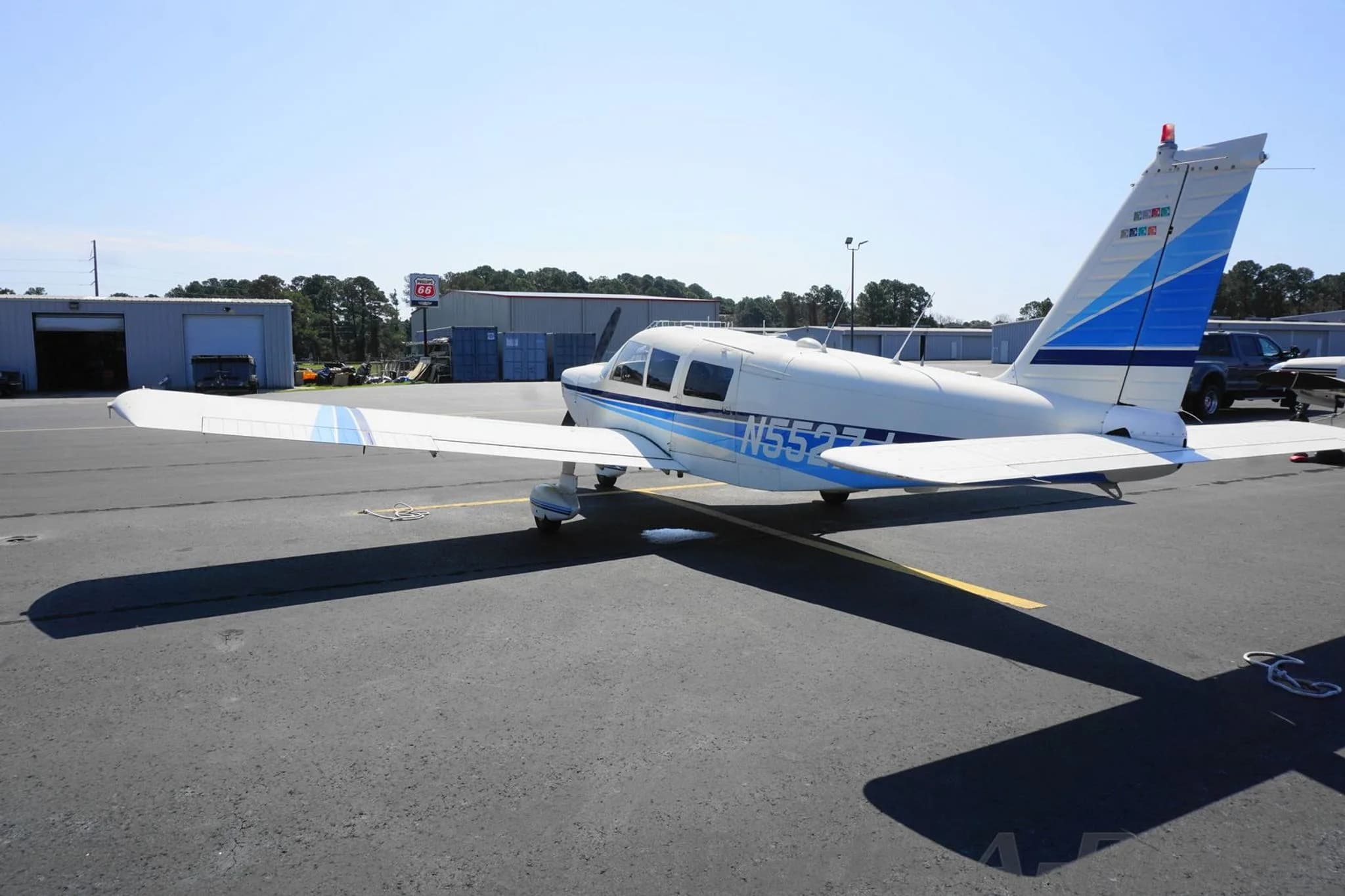 Rear-side view of the white N5527J single-engine propeller aircraft with blue stripes on an airport tarmac.