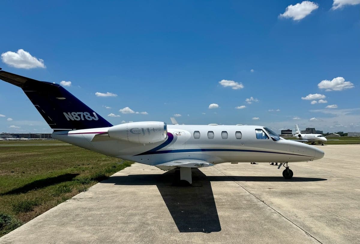 A white and purple Cessna Citation CJ1+ aircraft with registration N878J on the tarmac.