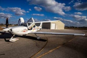 A Cirrus SR22 aircraft with a custom paint scheme is parked on the tarmac with its doors open.