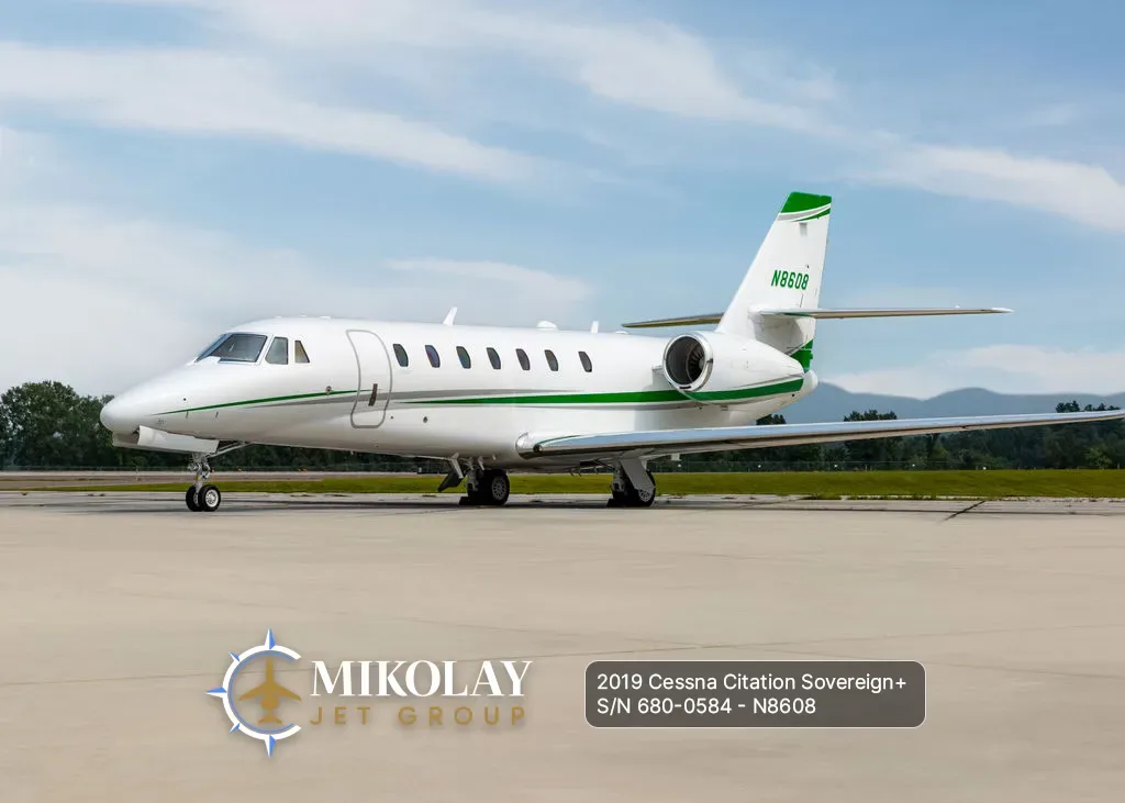 A white Cessna Citation Sovereign+ business jet with green accents on the tail and fuselage, parked on a tarmac on a clear day.