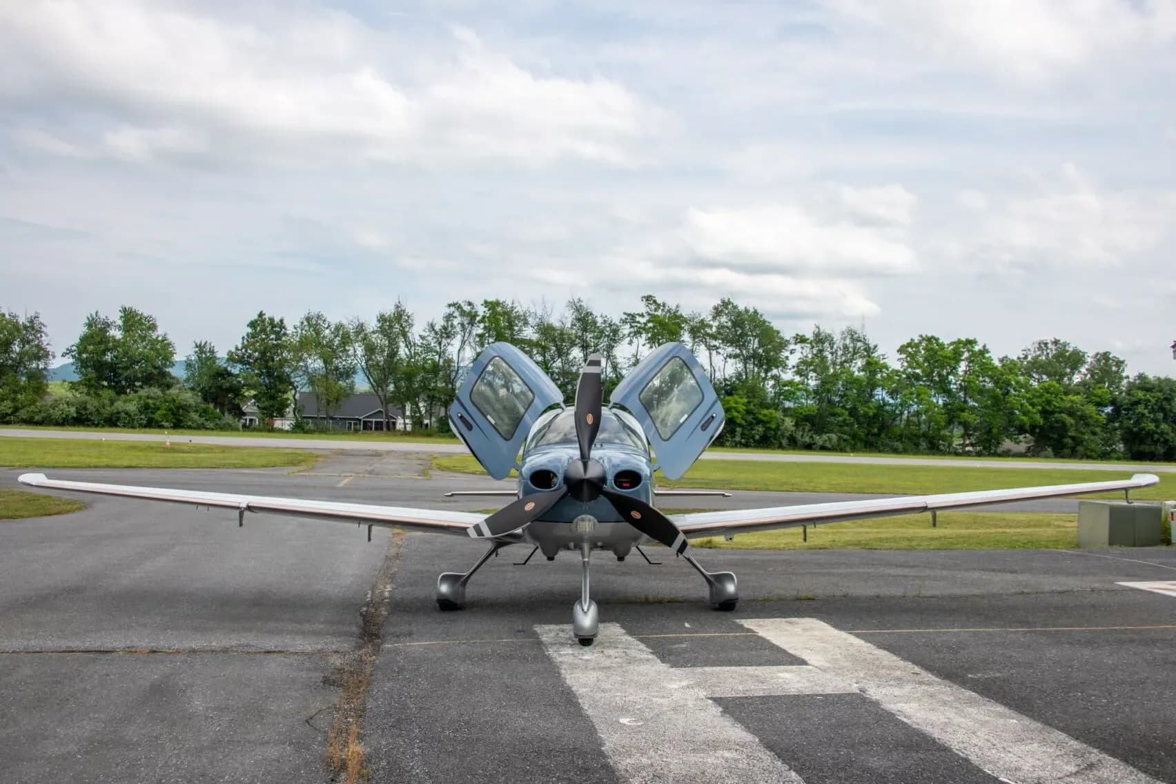 Front view of a blue Cirrus SR22T Carbon aircraft, N27MY, with its gull-wing doors open, on a runway.