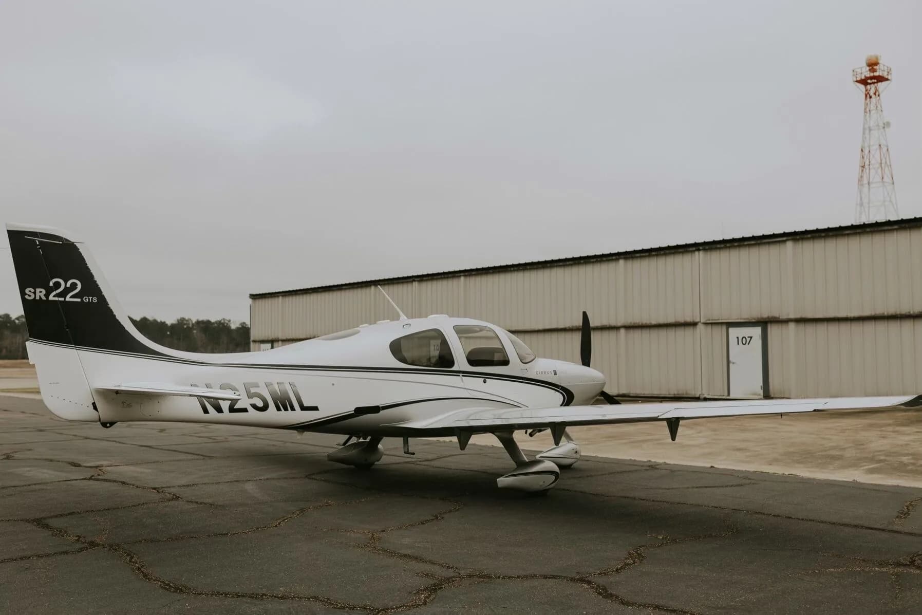 A three-quarter rear view of a silver Cirrus SR22 GTS aircraft with N25ML registration, parked on an asphalt ramp.