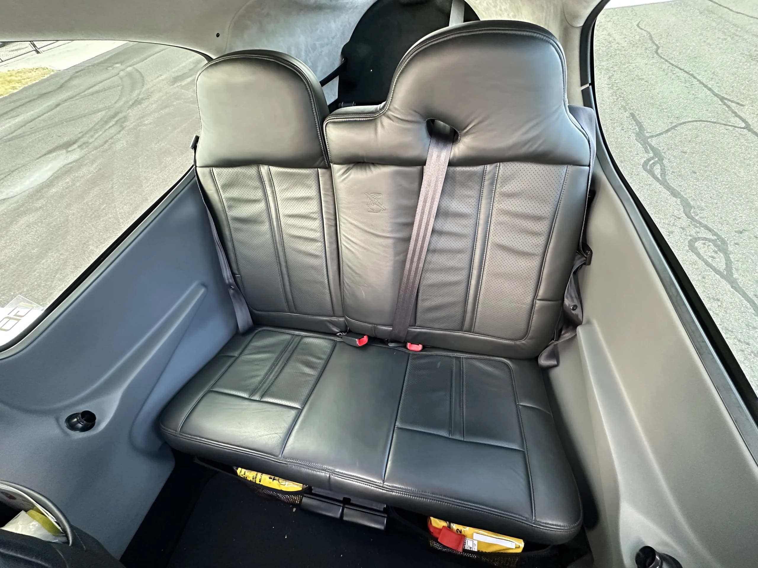 The rear two black leather seats of an aircraft cabin with seatbelts visible.