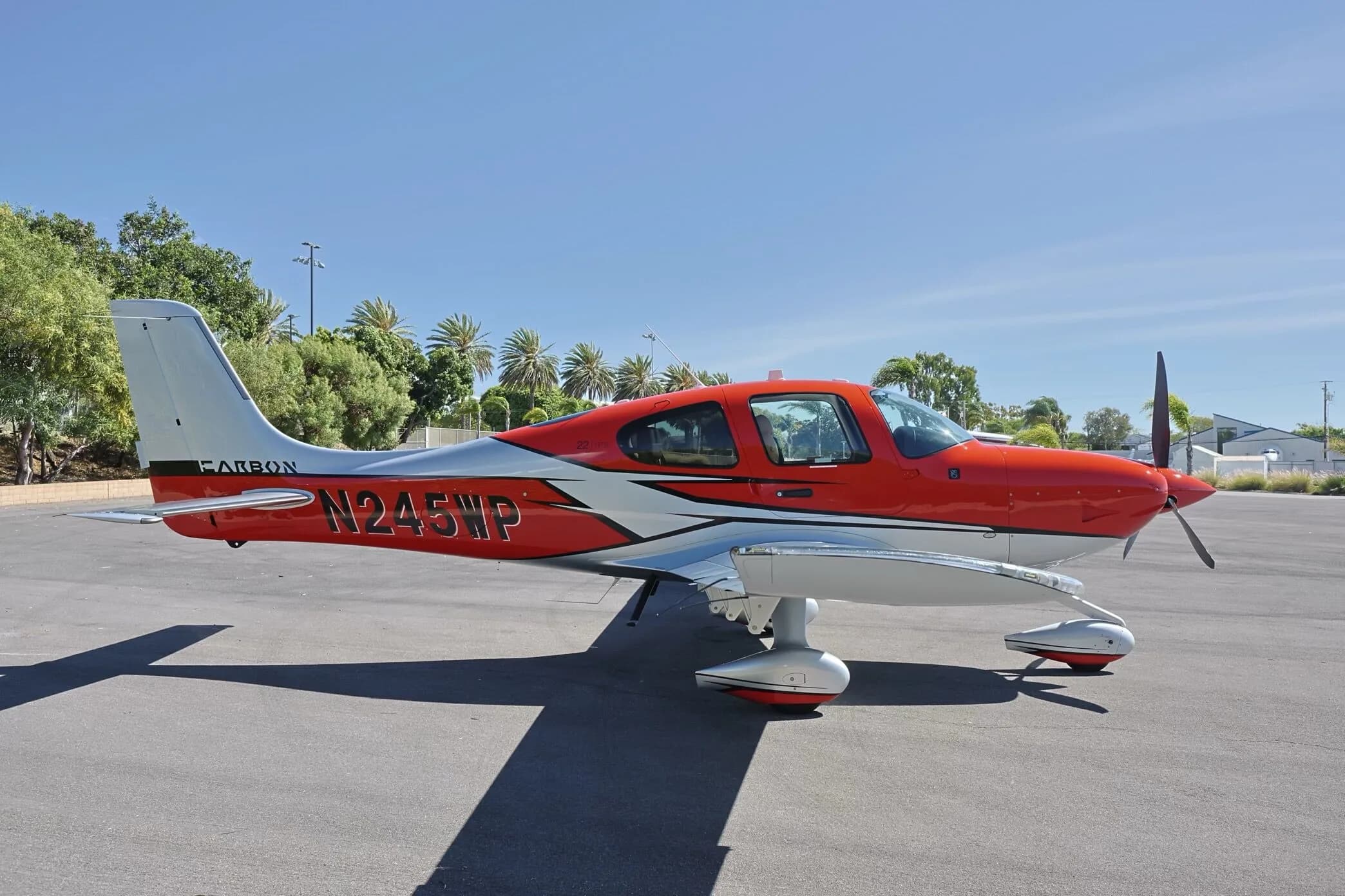 A red and silver single-engine propeller aircraft, N245WP, with 'CARBON' on its tail, parked on an asphalt tarmac on a sunny day.