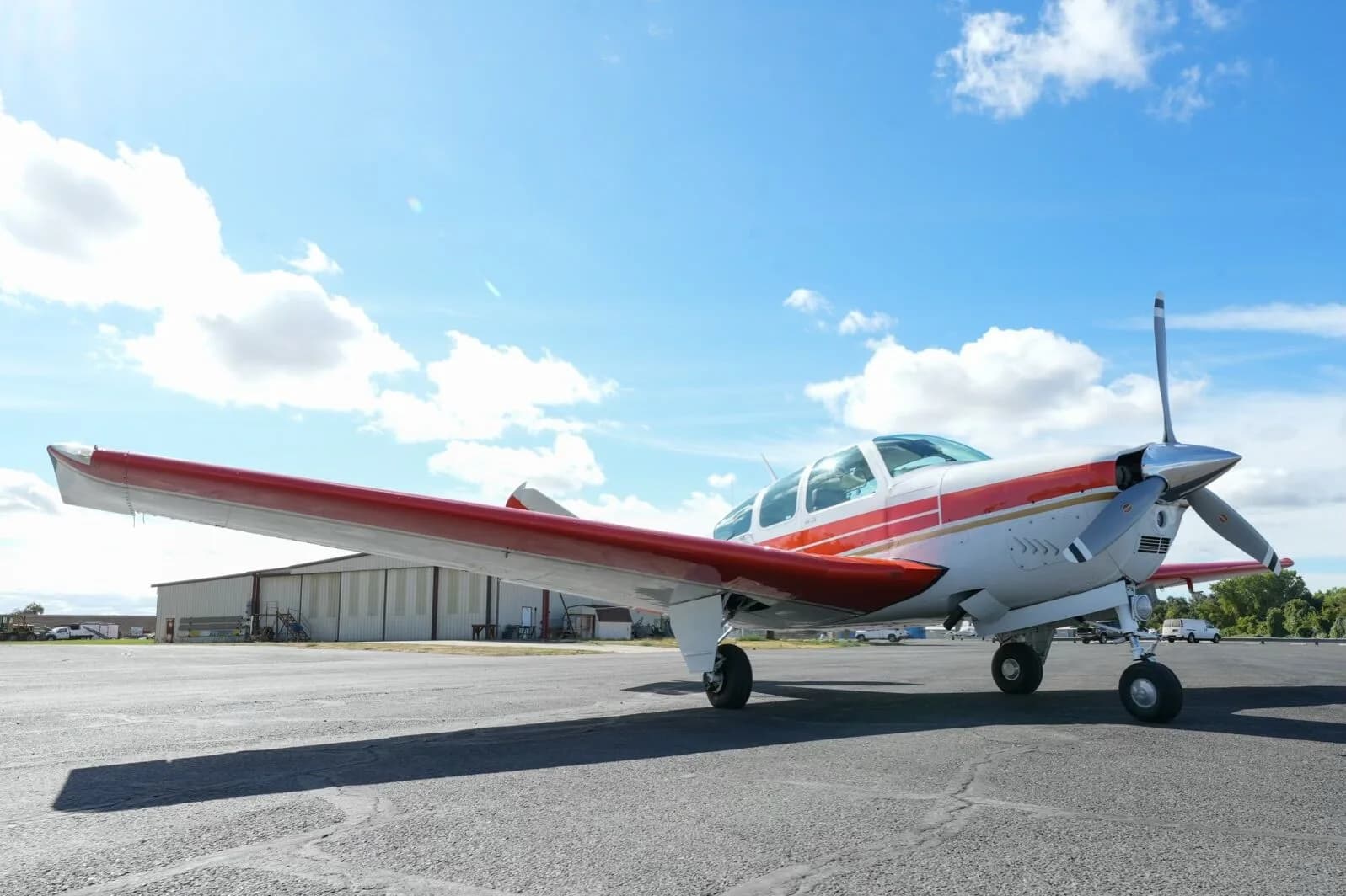 A low front view of the white and orange Beechcraft Bonanza N6AY parked on the tarmac.