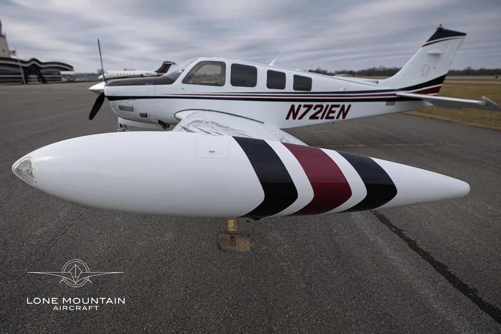 A close-up view of the right wingtip tank of the N721EN aircraft, showing its white, black, and red stripe paint scheme.
