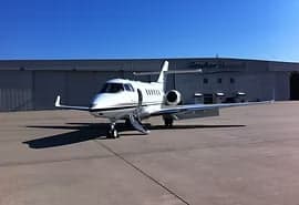 A white private jet parked in front of a hangar with its door open.