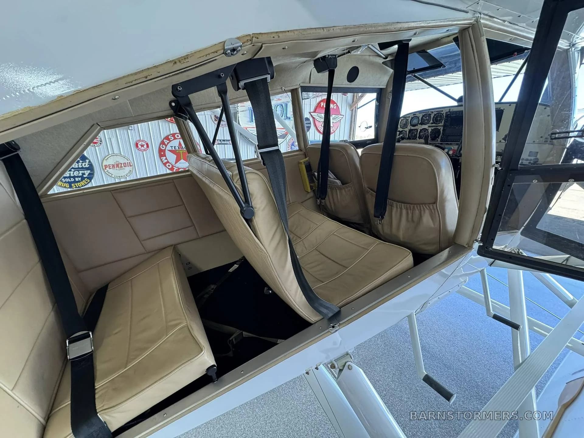 The tan interior cabin of a floatplane, showing two rows of seats with seatbelts, looking towards the cockpit.