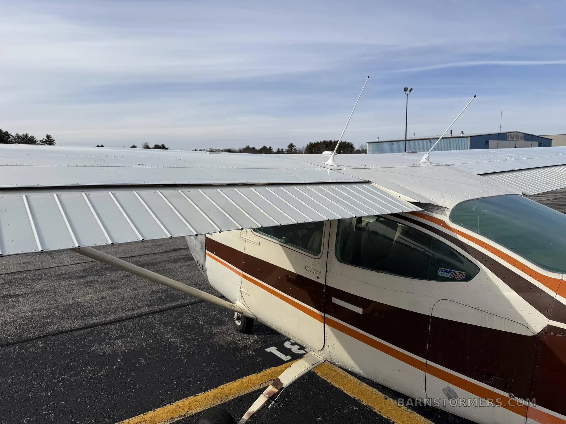 An overhead view of the wing and fuselage of a white and brown aircraft parked on an asphalt ramp.