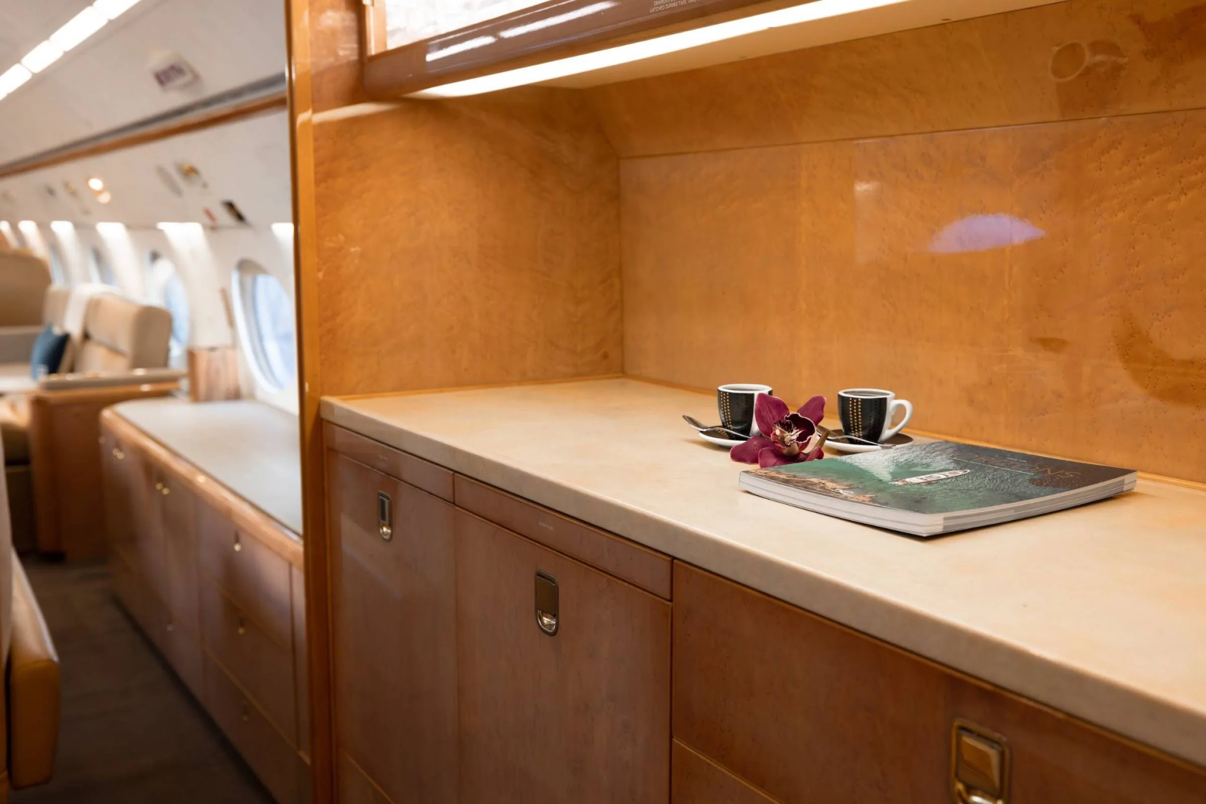 A close-up of a private jet's wooden credenza with two espresso cups, an orchid, and a magazine.