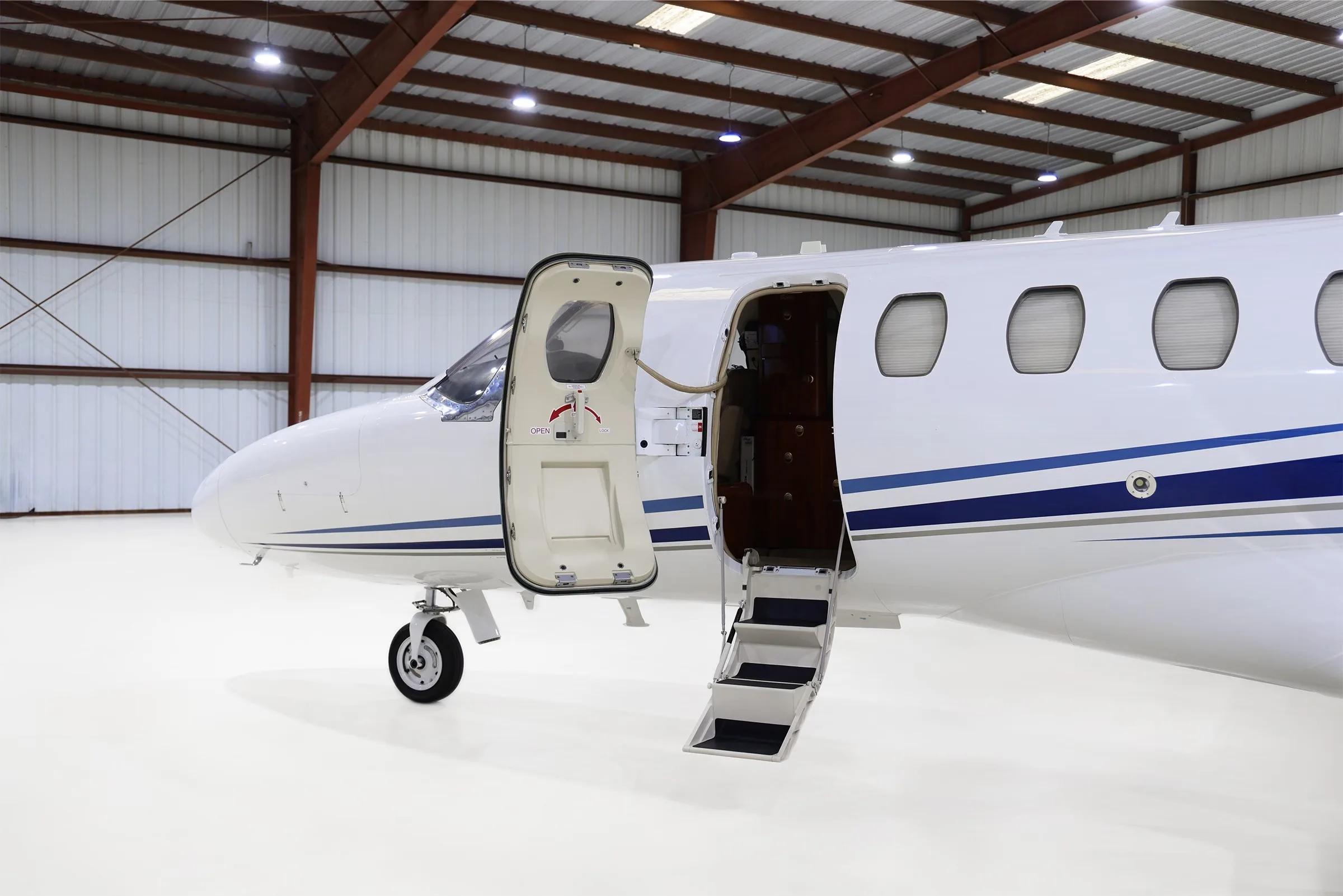 A close-up of the open main cabin door and airstairs of a white Cessna Citation CJ2+ (N525WD) with blue stripes.
