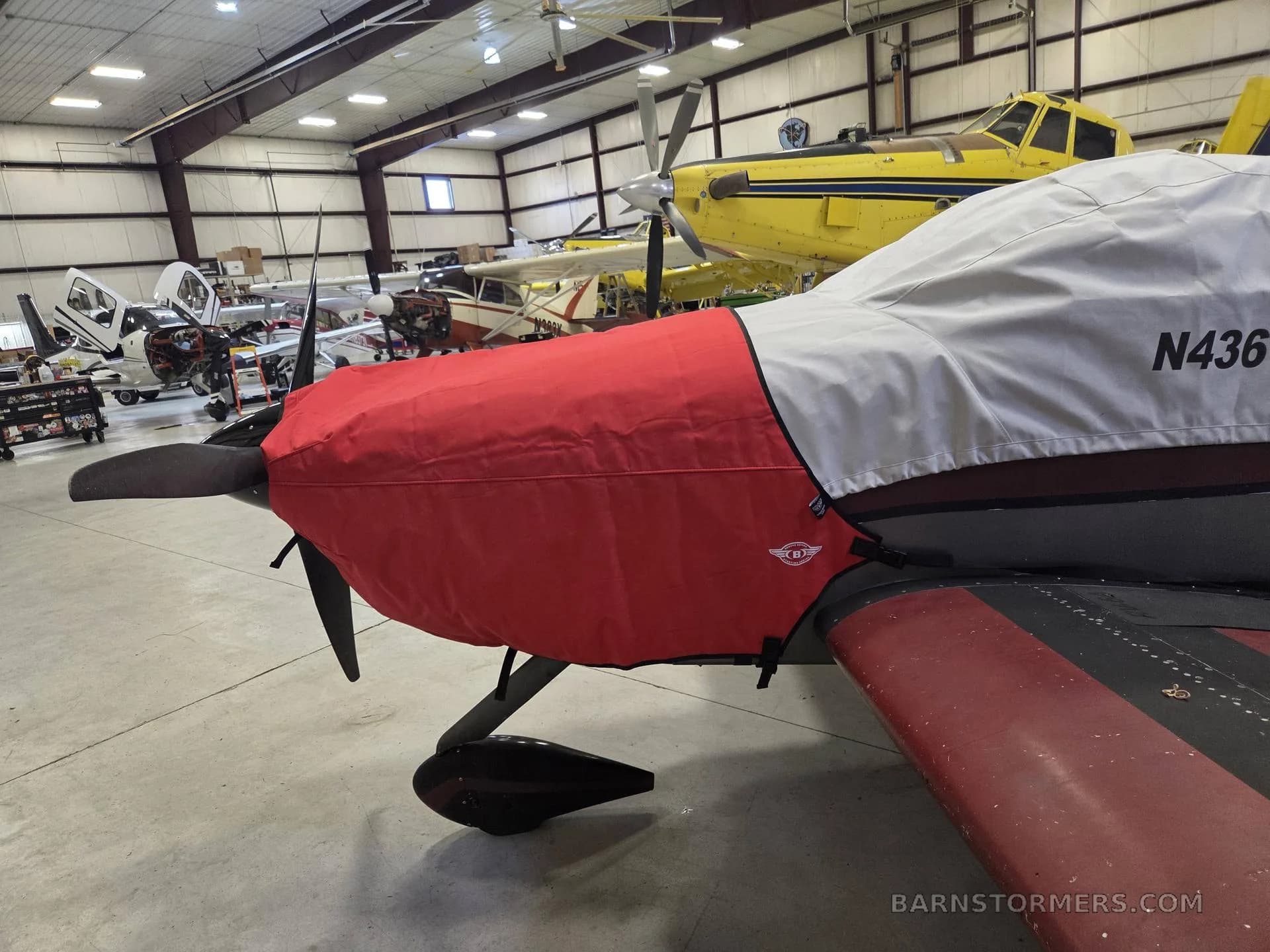 The front of an N4361V aircraft covered with a red and white engine cover, parked inside a hangar.