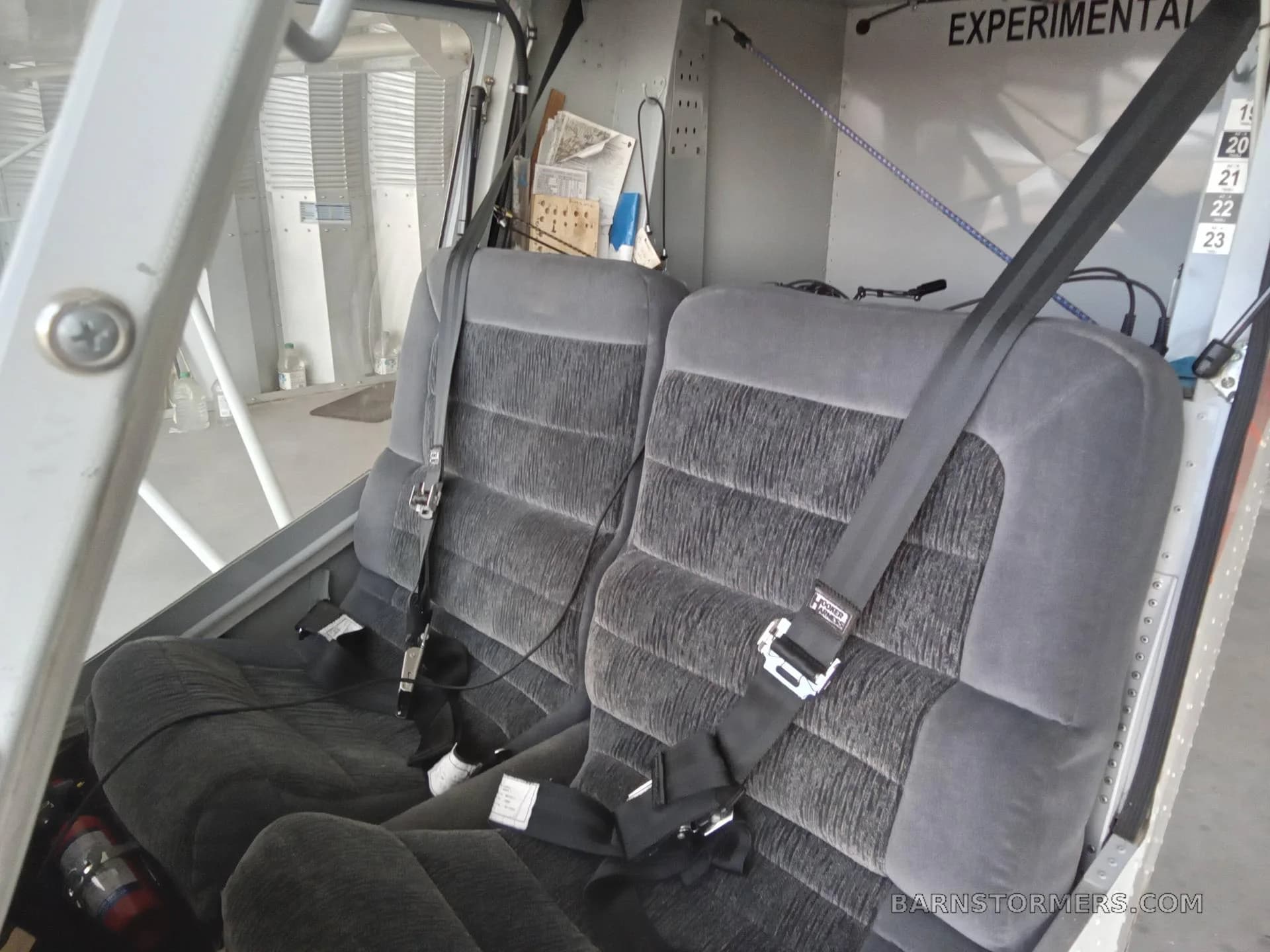 The gray fabric seats with seatbelts inside a small aircraft, with "EXPERIMENTAL" visible on the wall.