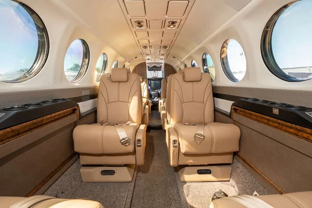 View down the aisle of the aircraft cabin with tan leather seats and large windows.