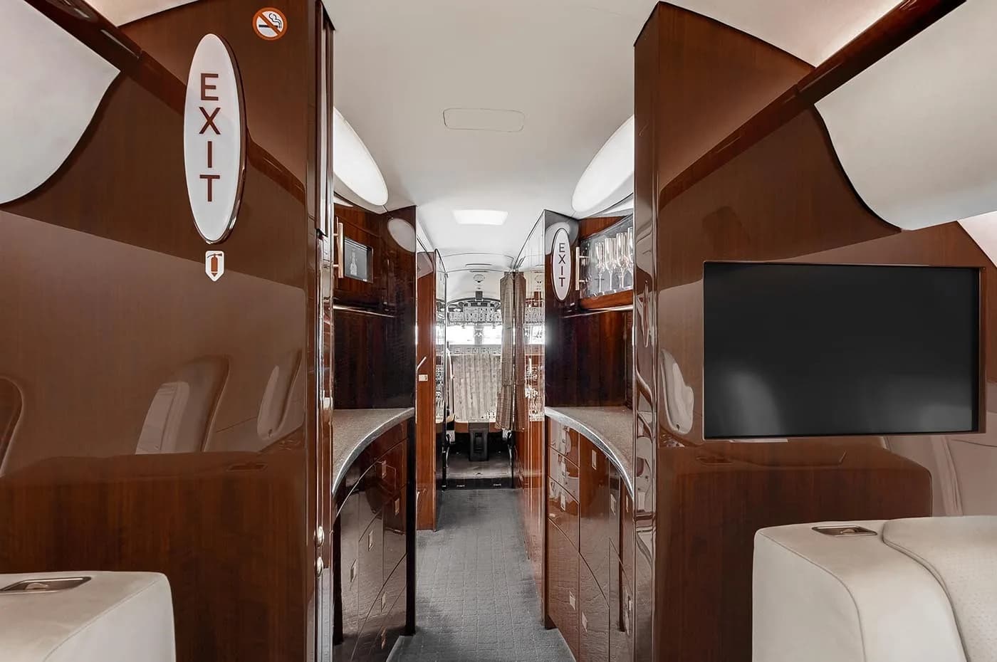 The galley area of a business jet, featuring dark wood cabinetry, a counter, and a mounted screen.