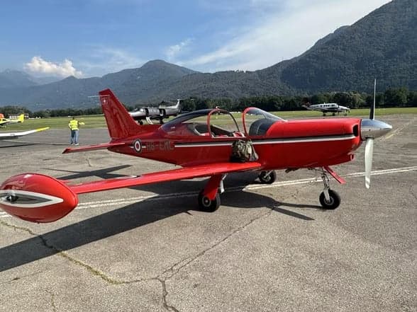 A red aircraft, HB-EML, parked on the tarmac in front of a hangar.