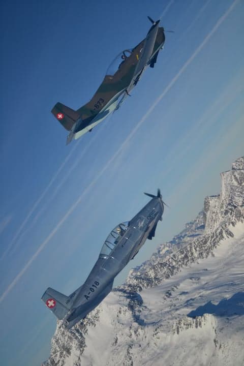 Two Pilatus PC-7 aircraft in flight over a snowy landscape.