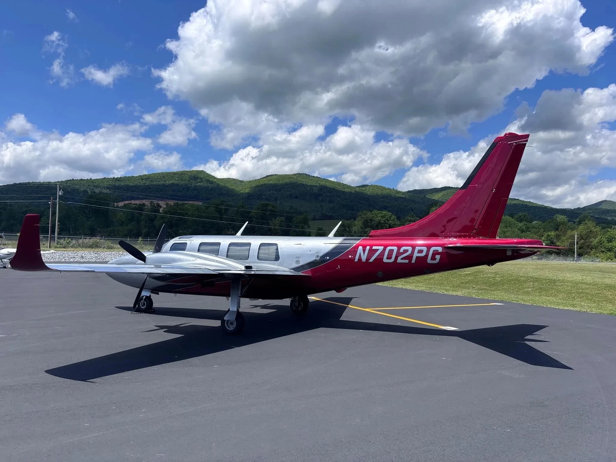 A side view of a silver and red twin-engine Aerostar aircraft (N702PG) parked on an airfield.