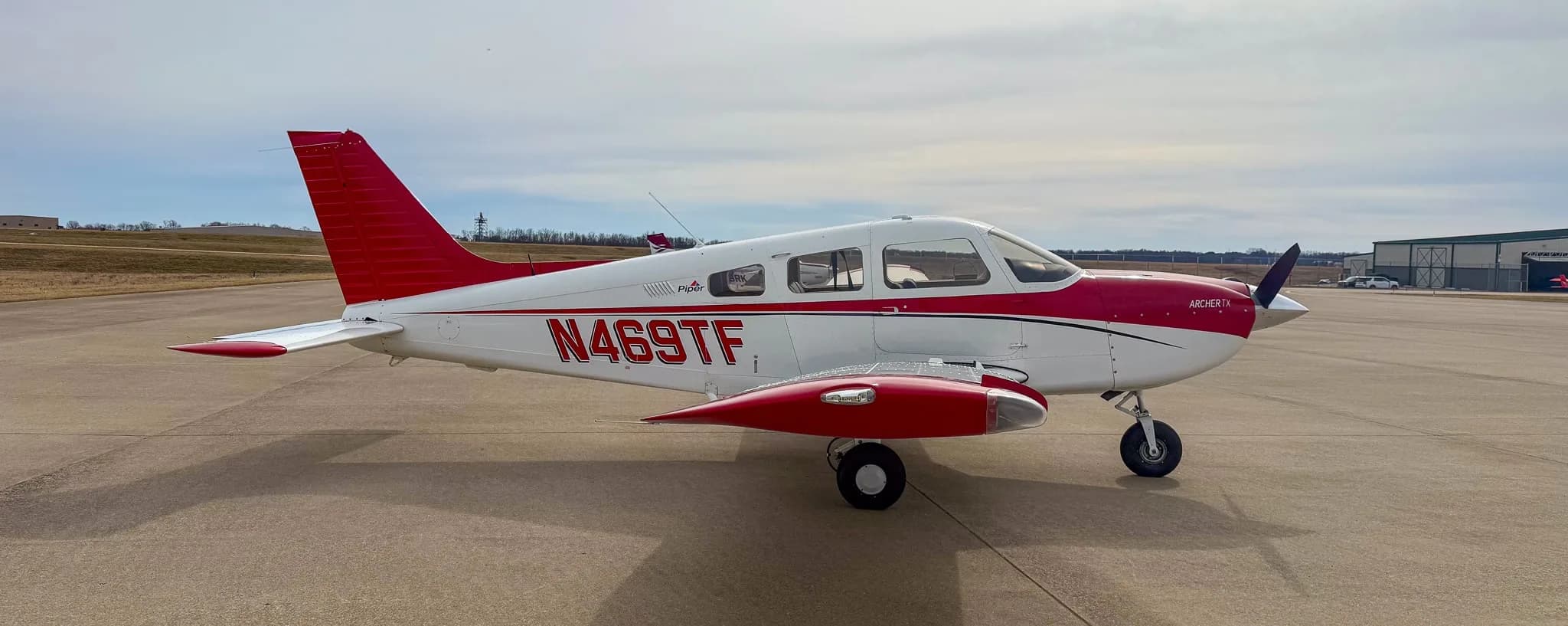 A side view of a white and red Piper Archer TX aircraft, N469TF, with red wheel pants, on an airfield.