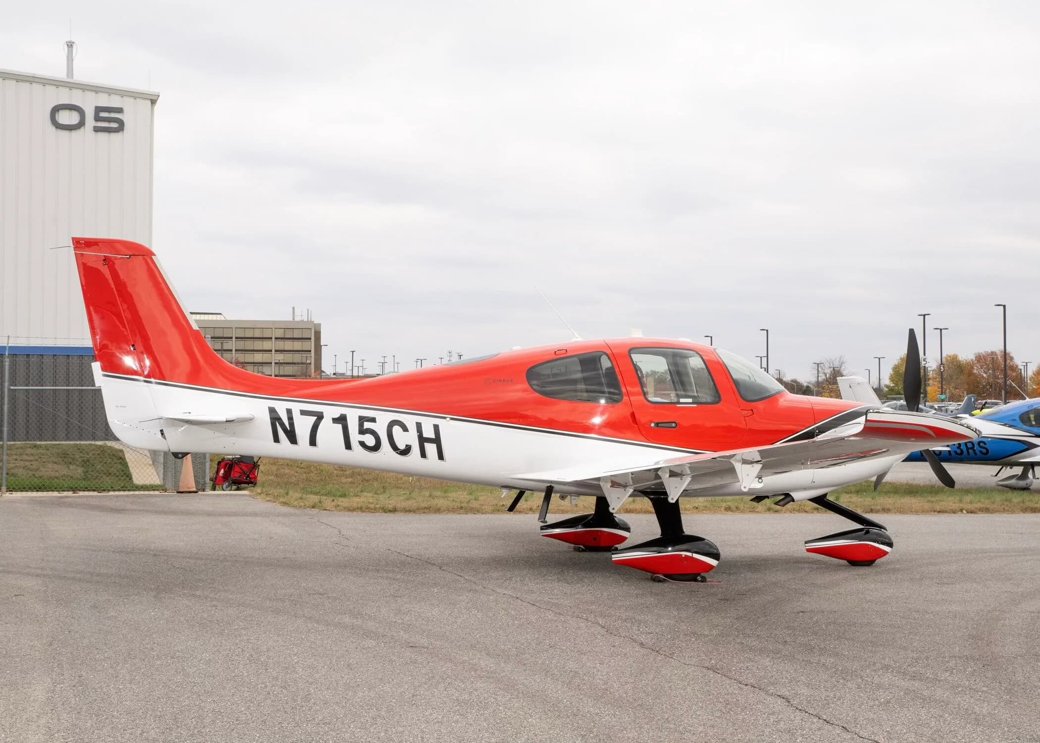 A red and white Cirrus SR22 aircraft with registration N715CH parked on an airfield next to a hangar.