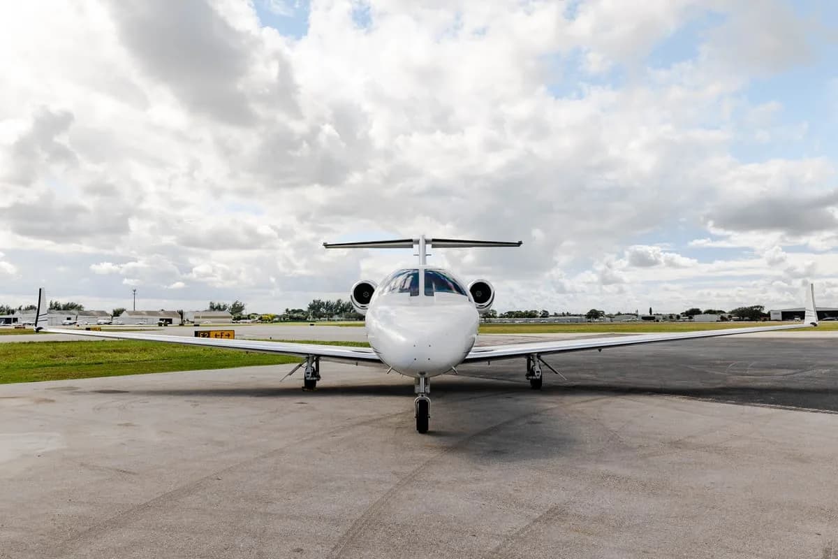 Front view of a white Cessna Citation private jet parked on the tarmac under a cloudy sky.