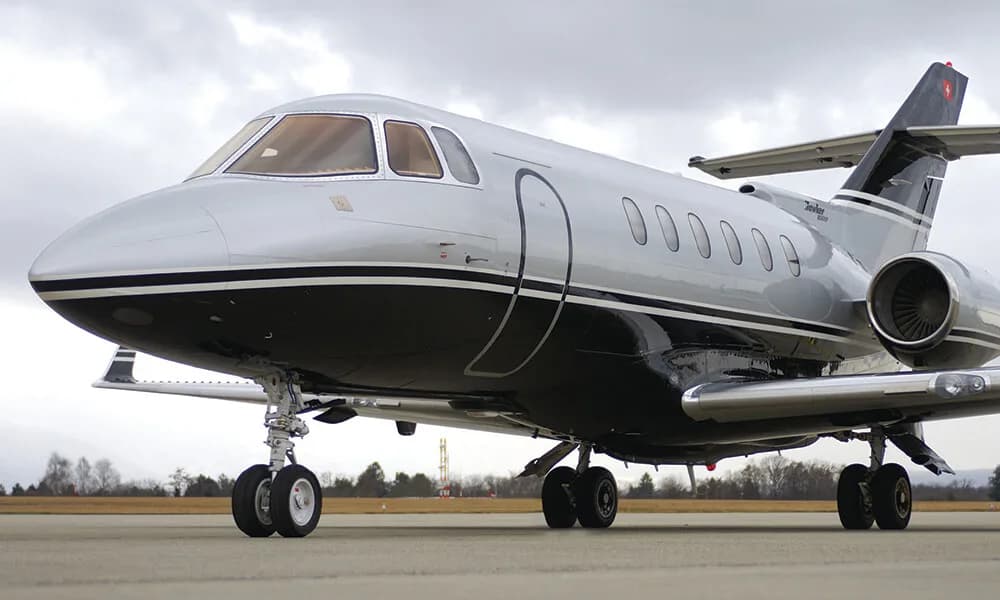 A front-side view of a silver and black Hawker 800XP business jet on an airfield.