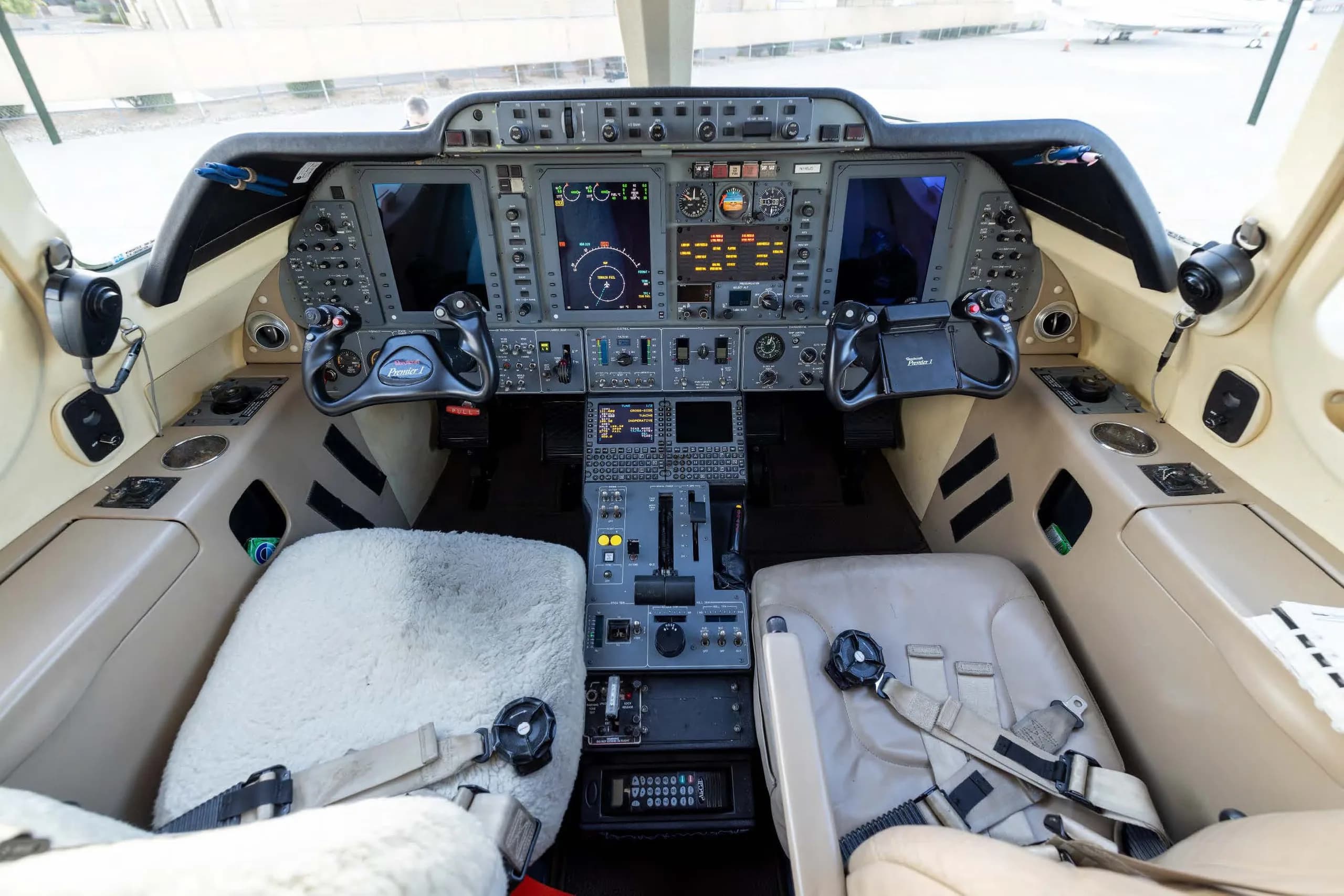 A wide view of the modern glass cockpit of a business jet, featuring multiple display screens and control yokes.