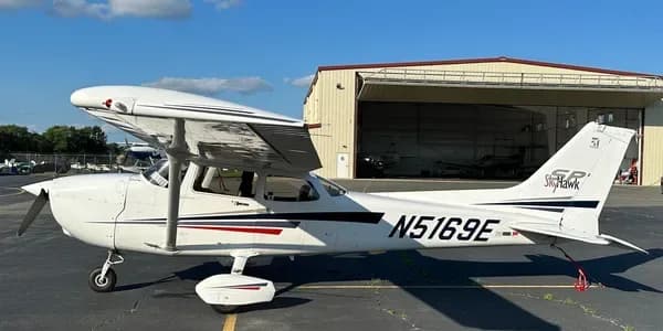 A white Cessna aircraft with blue and grey stripes, registration N53576, parked on an tarmac.