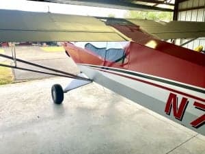 Partial side view of the red and silver Carbon Cub N7XU inside a hangar.
