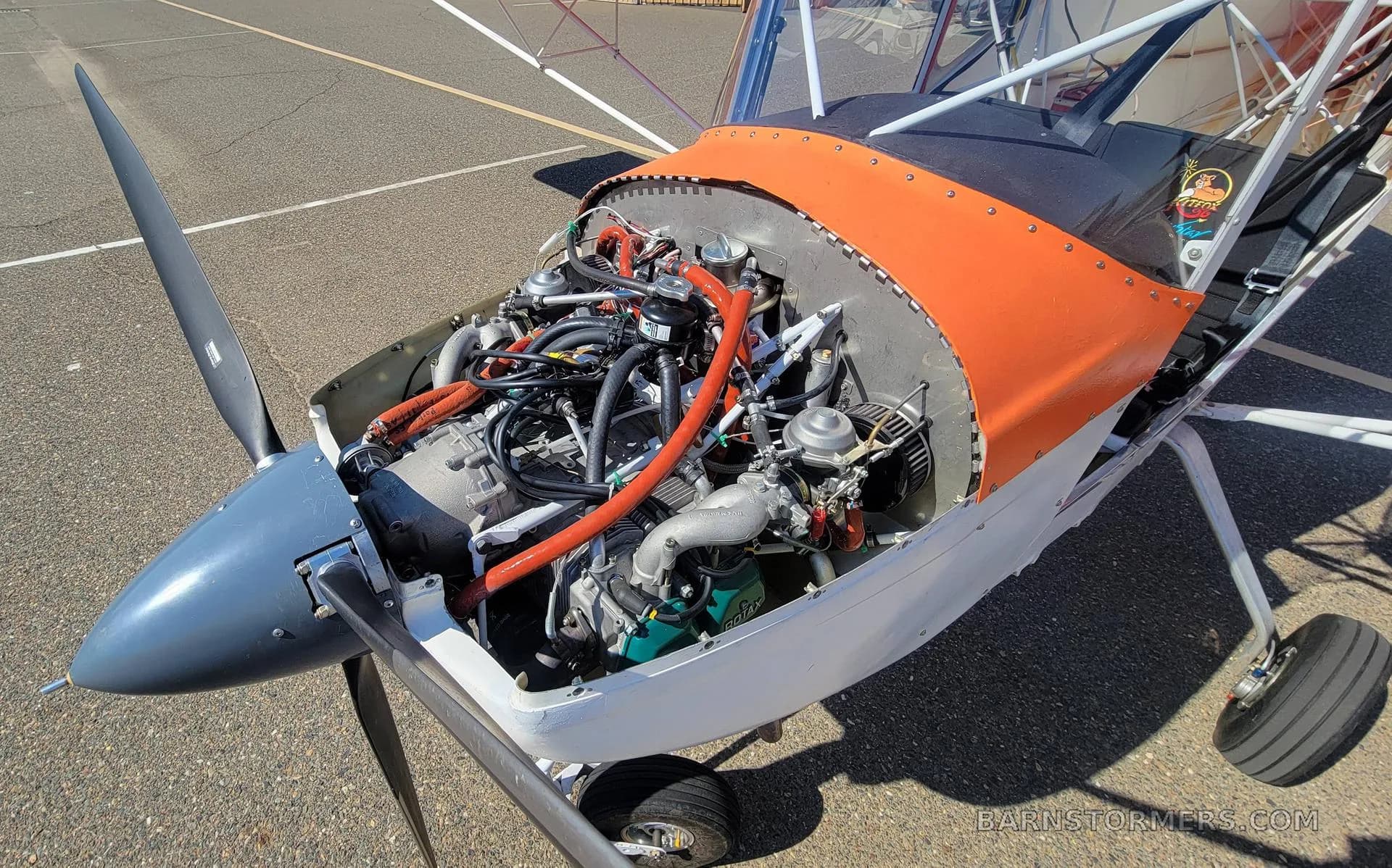 The exposed engine compartment of the aircraft, showing the engine, hoses, and propeller spinner.