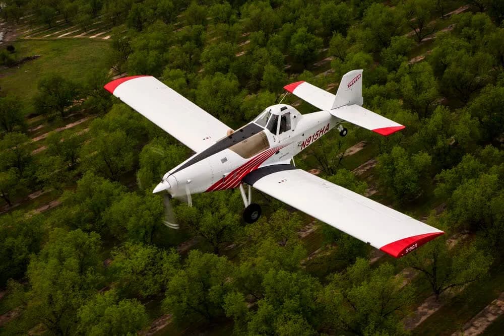 Aerial view of a white and red Air Tractor crop duster flying over trees.