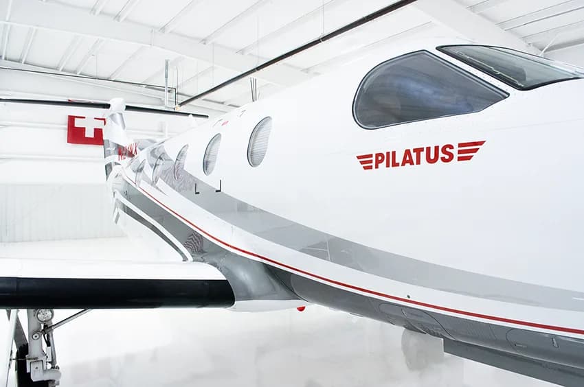 A close-up view of the tail and rear fuselage of a white Pilatus PC-12NG aircraft with gray and black stripes and registration N21NX.