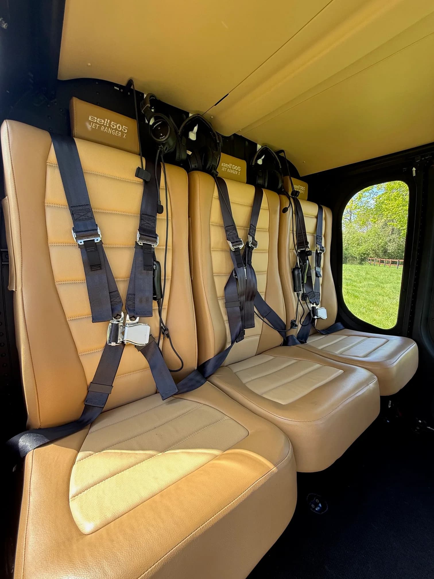 Three tan leather rear seats with harnesses are visible inside the cabin of a Bell 505 Jet Ranger X helicopter.