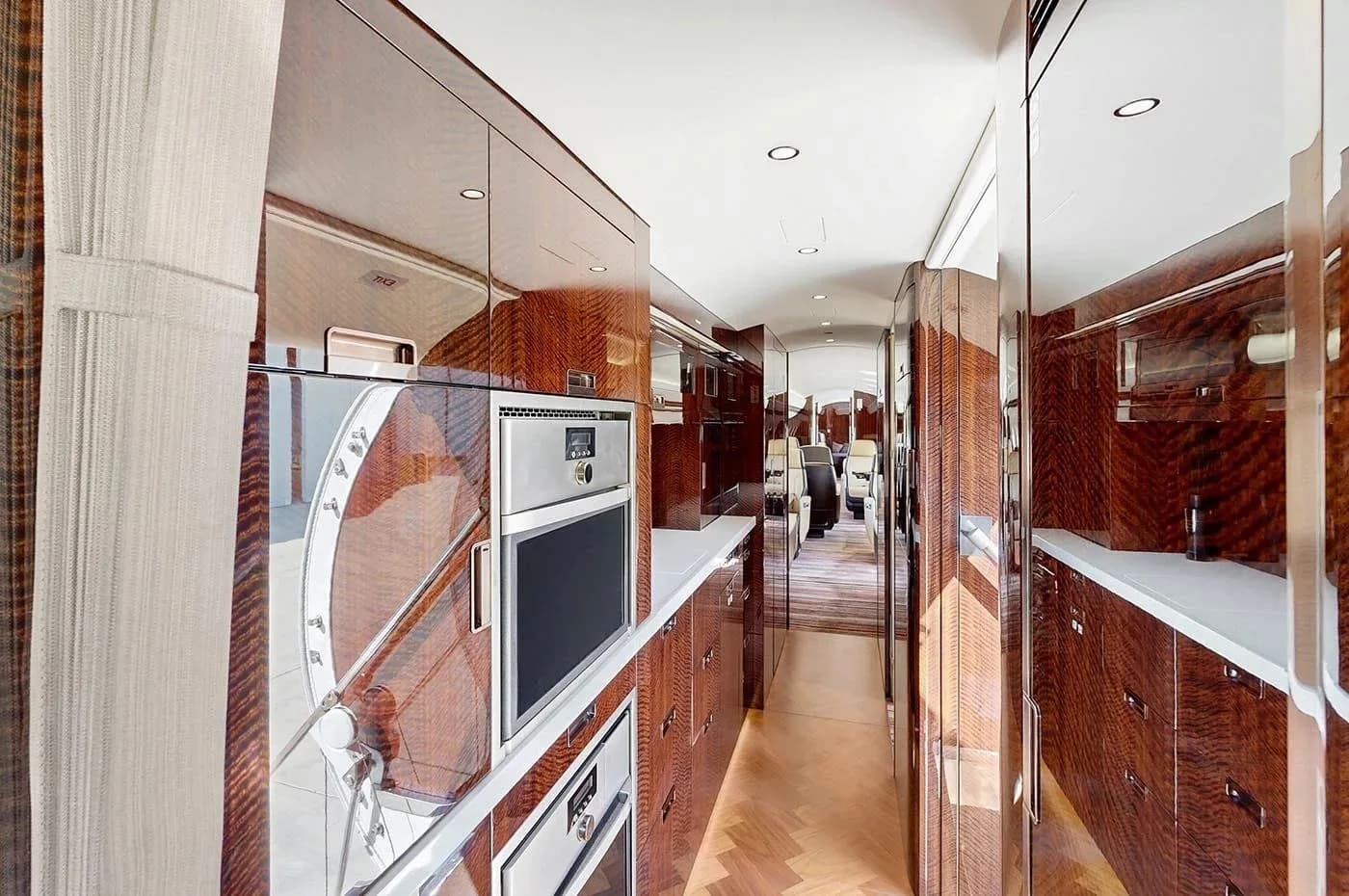 The galley of the Bombardier Global business jet, featuring polished dark wood cabinetry, a microwave, and an oven.