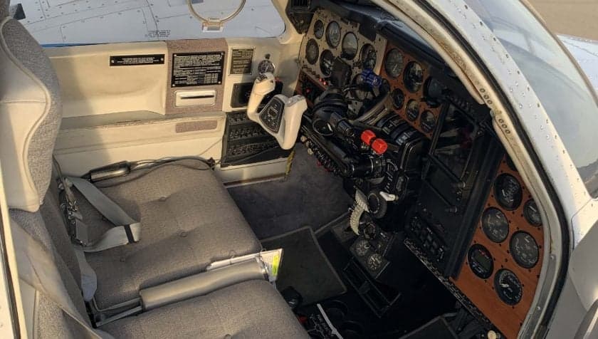 View of the cockpit of an aircraft with gray seats and a wood-paneled instrument panel.