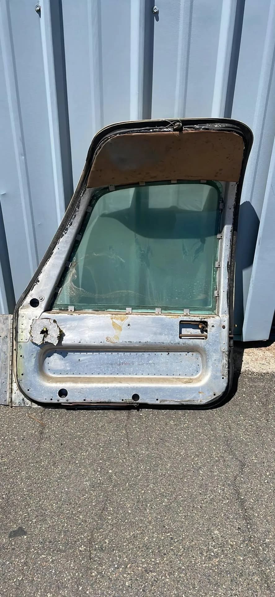 A close-up view of a detached, weathered aircraft door with a window.