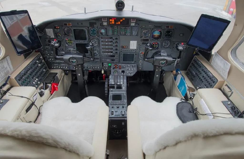 A detailed view of the private jet's cockpit, featuring a complex instrument panel and two pilot seats with white sheepskin covers.
