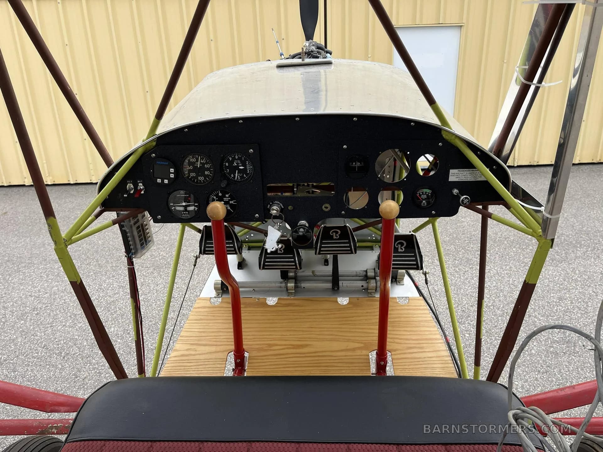 A view from the pilot's seat showing the basic instrument panel, rudder pedals, and control sticks of an open-frame ultralight aircraft.