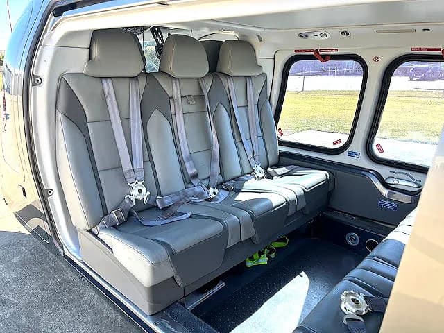Interior view of the helicopter cabin with gray leather seats and seatbelts.