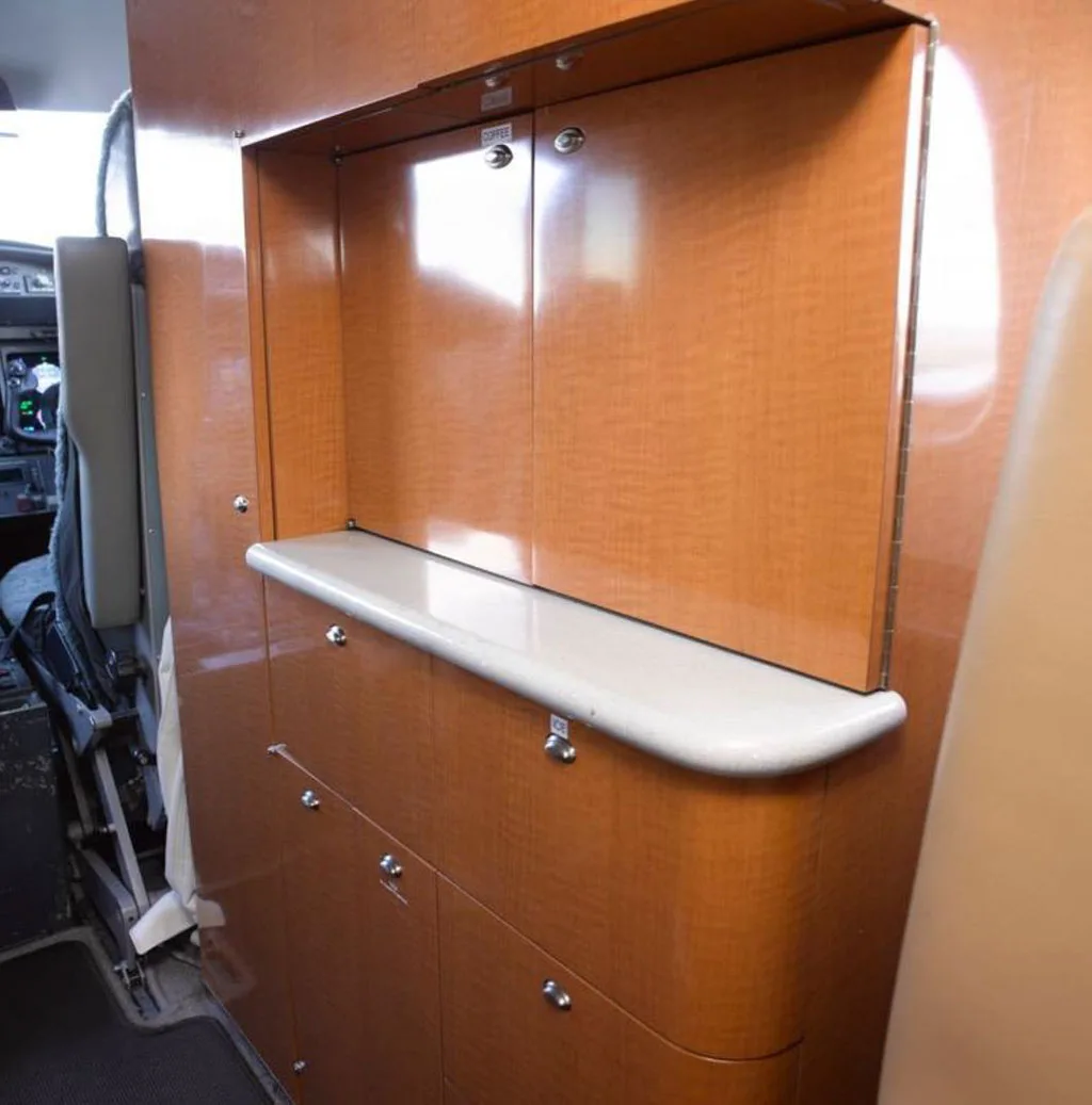 A wooden galley or storage unit with a countertop is visible in the aircraft cabin, with the cockpit partially seen on the left.