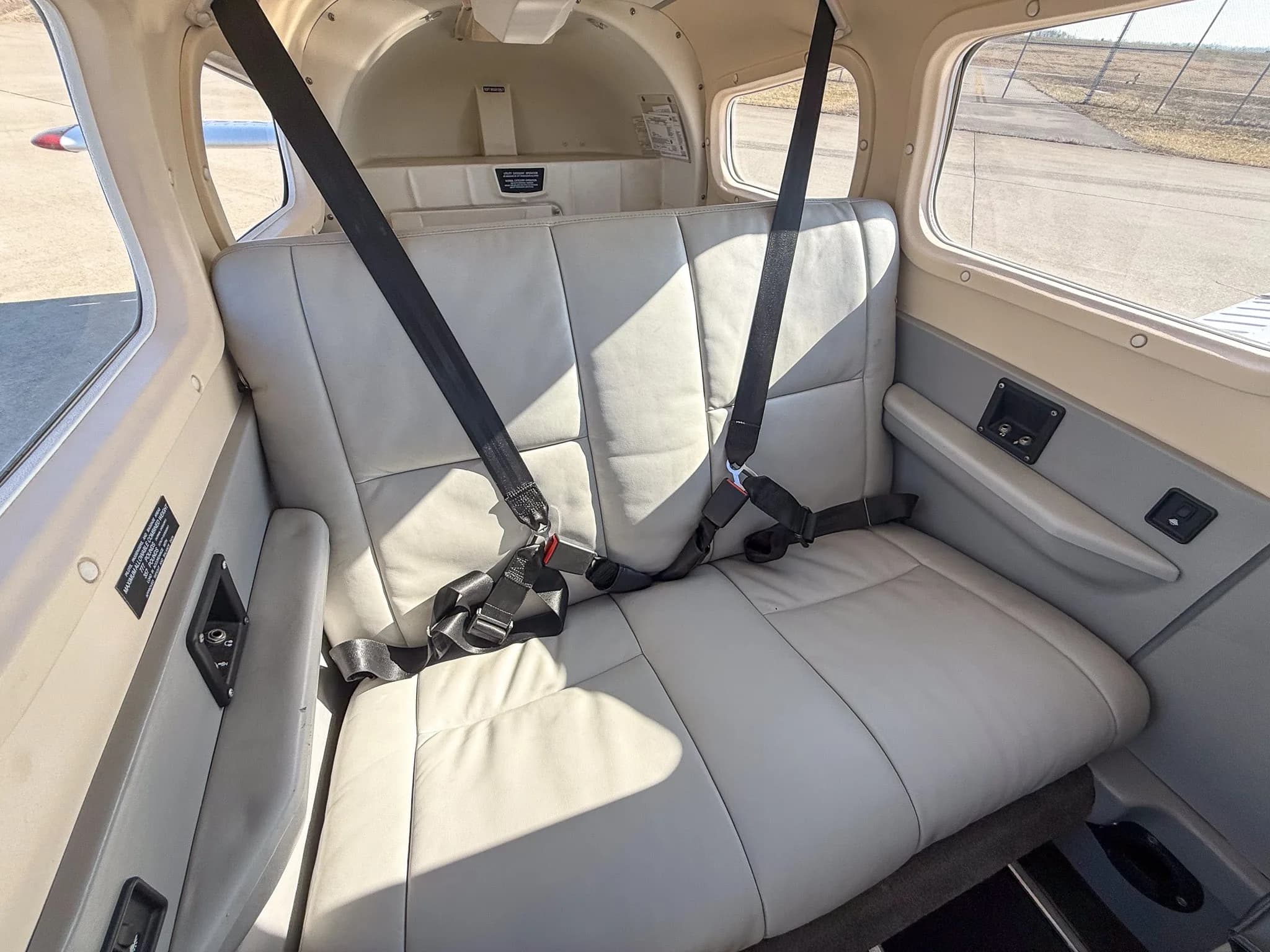 The light gray leather rear passenger seats of a Piper Archer TX cabin, with sunlight streaming in.