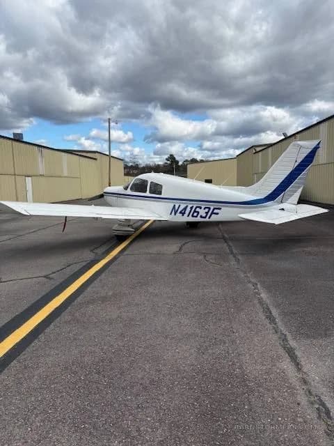 A side view of a white single-engine propeller aircraft with blue stripes (N4163F) parked on an asphalt tarmac.