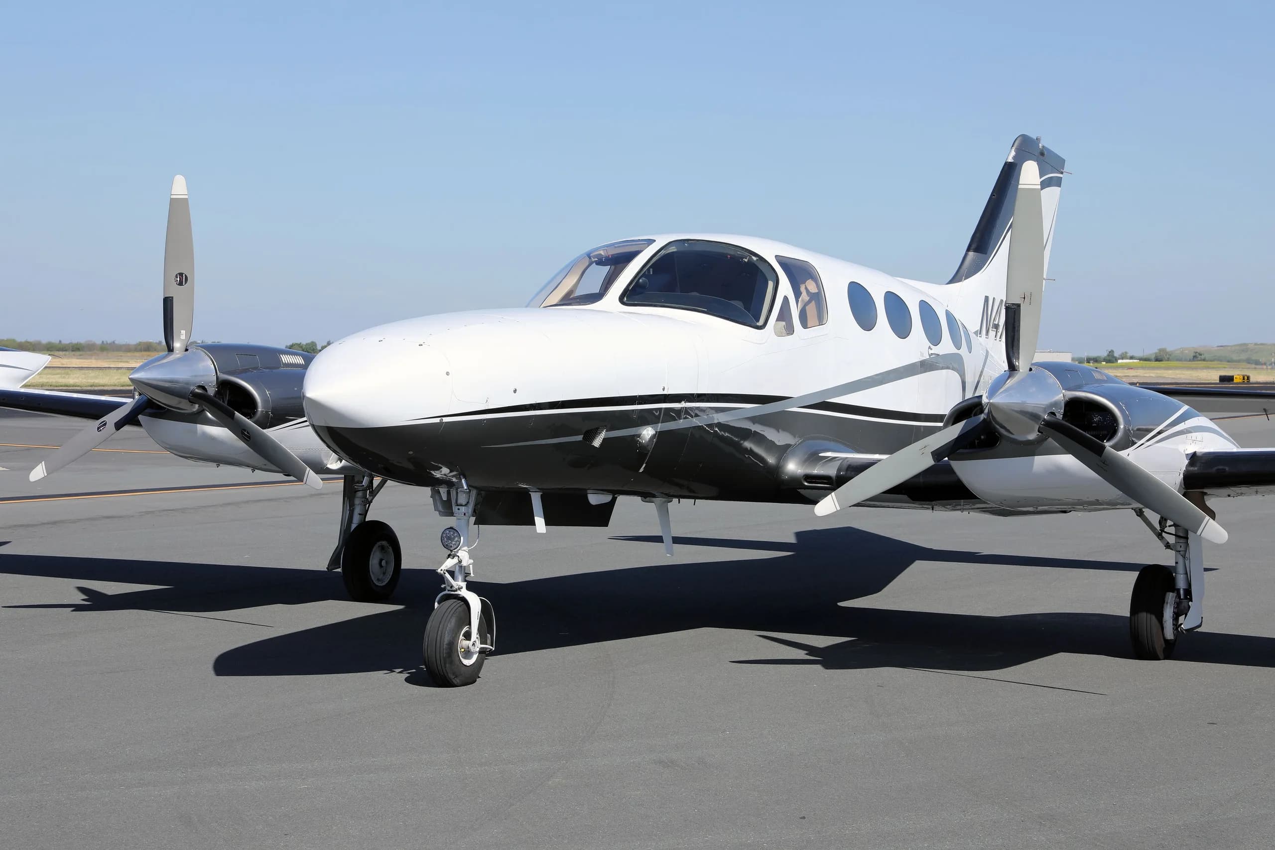 A front-quarter view of the white and grey twin-engine Cessna 414 Chancellor aircraft, N477MG, parked on an asphalt tarmac.